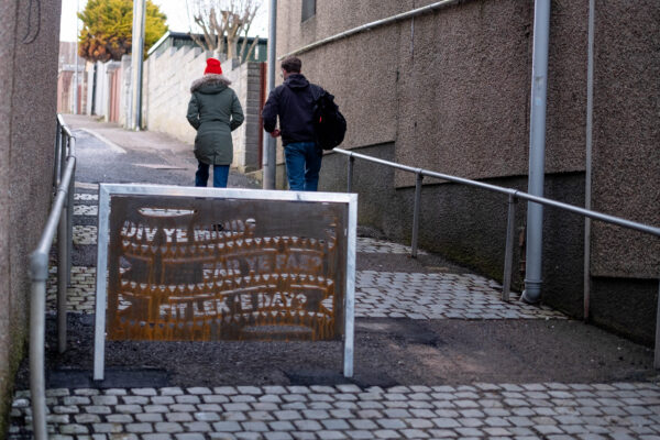 2 adults walk away from camera in background with a poem depicted on a barrier in foreground